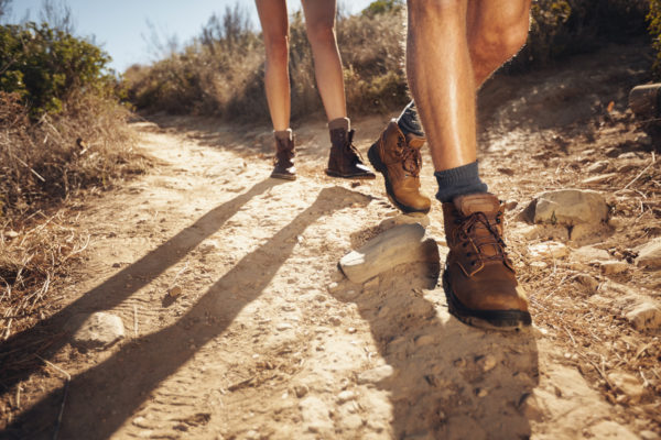 Close-up of legs of young hikers walking on the country path. Young couple trail waking. Focus on hiking shoes.